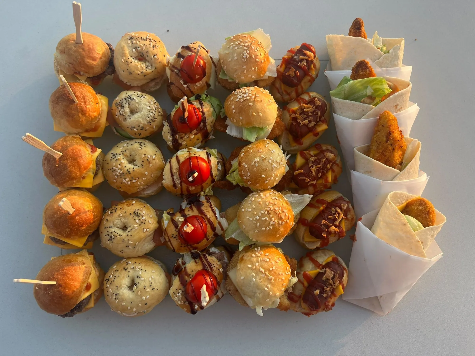 Vue de dessus d'un plateau de mini-burgers, mini-bagels et wraps en cornets