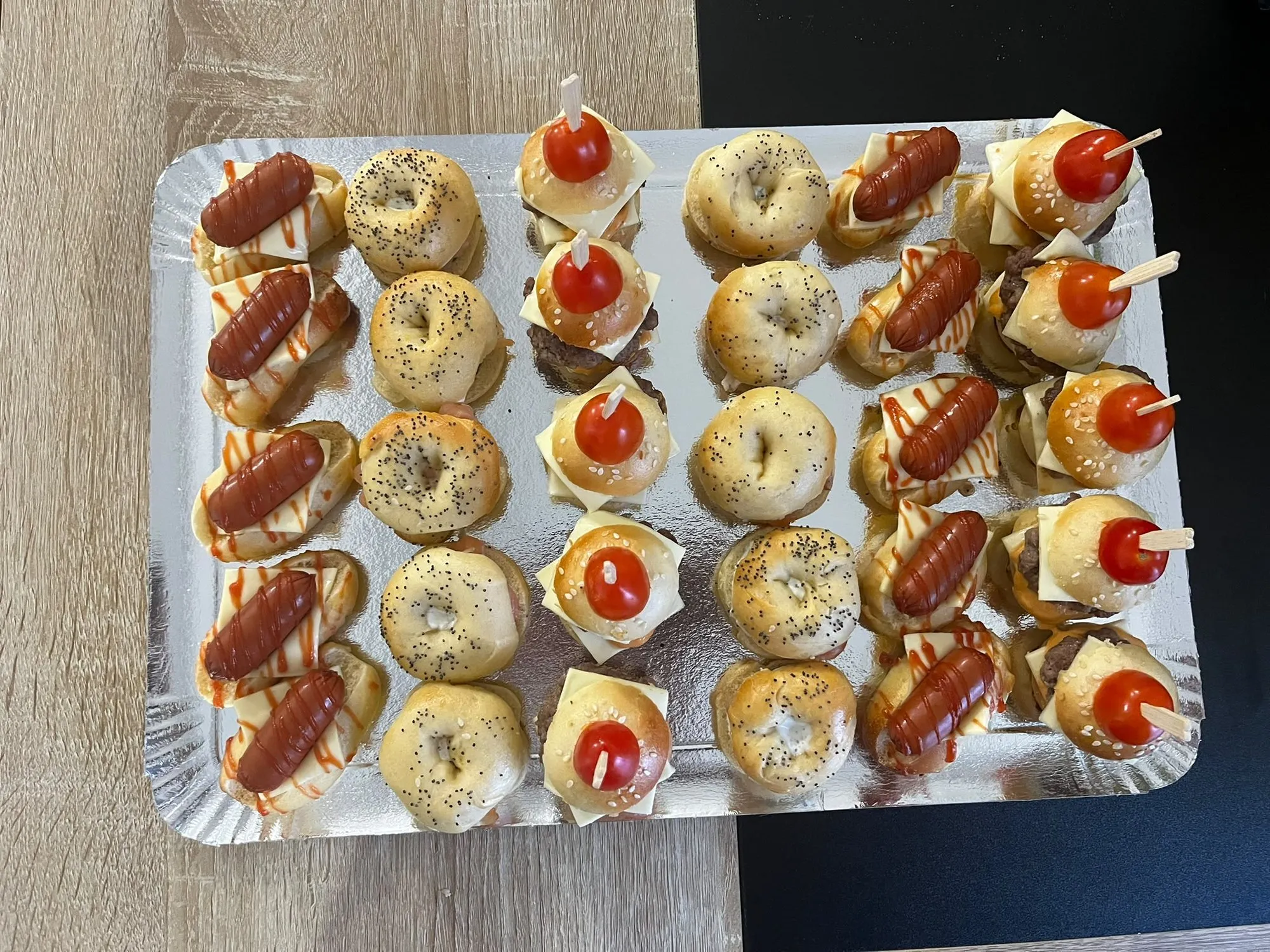 Vue de dessus d'un plateau de bouchées cocktail alternant mini-bagels, mini hot-dogs et brochettes
